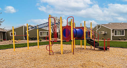 A playground with a red and blue slide, yellow poles, and a black ramp.