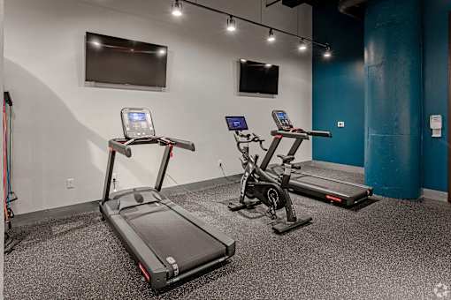 Two treadmills are in a room with a blue wall and a television.