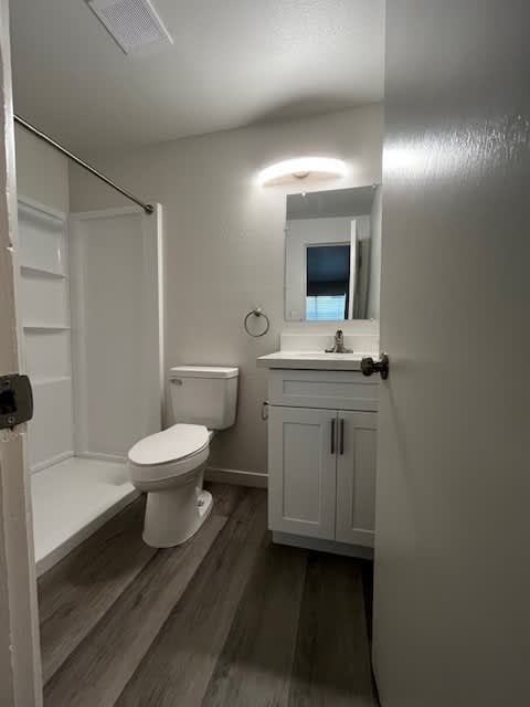 A white toilet is in a small bathroom with a white cabinet and a mirror.