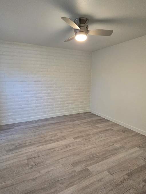 A room with a ceiling fan and light, wooden flooring, and white walls.