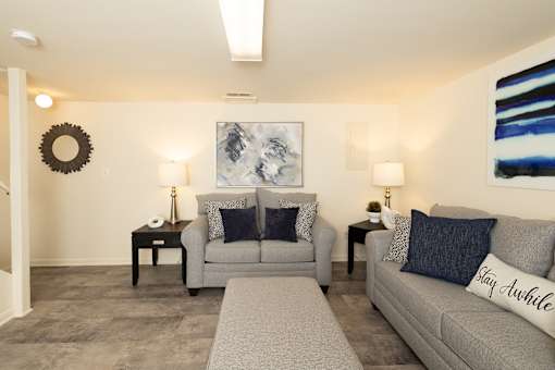 A living room with a grey couch and a large painting on the wall.