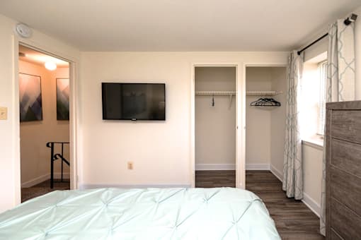 A bedroom with a bed, a TV, and a window with curtains at Kingston Townhomes, Baltimore, MD