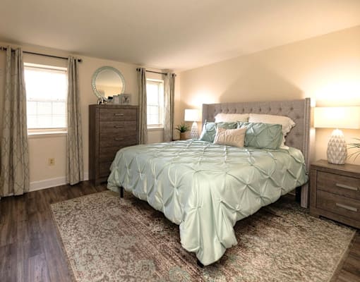 A bedroom with a bed, nightstand, and window at Kingston Townhomes, Baltimore, MD