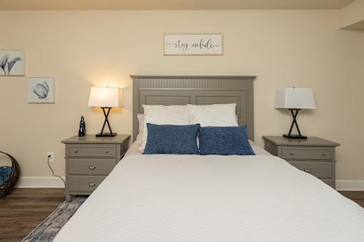 A bedroom with a bed, two lamps, and a wall art.at Deer Park Apartments, Randallstown, 21133