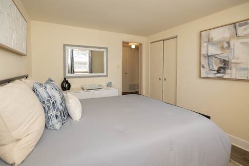 A bedroom with a bed, a mirror, and a painting on the wall.