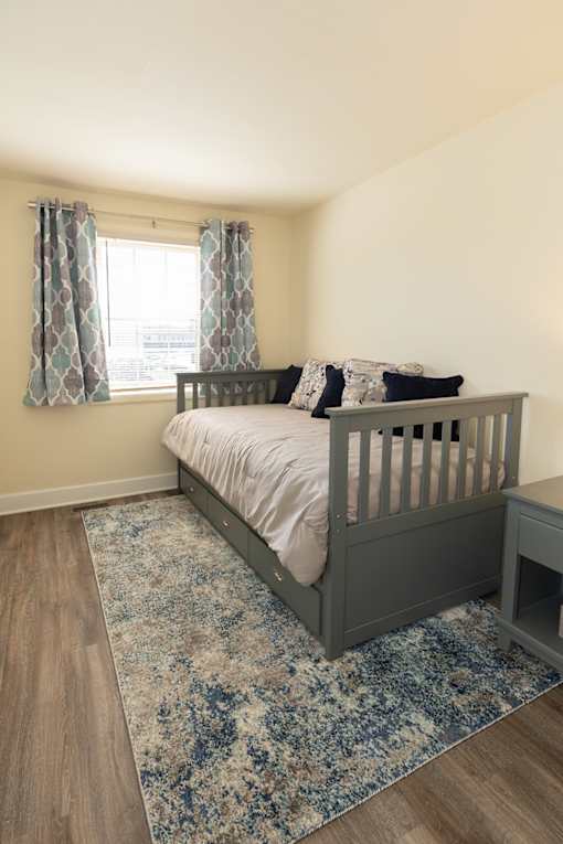 A baby's room with a crib, a rug, and a window with curtains