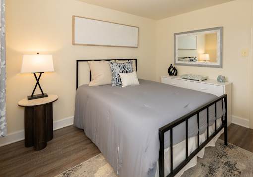 A bedroom with a bed, nightstand, and lamp at Hyde Park Apartments*, Essex, MD 21221