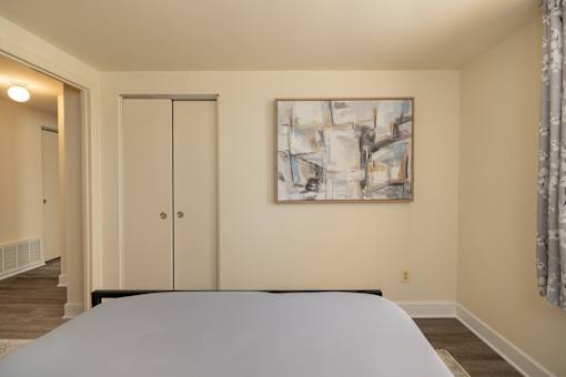 A bedroom with a bed, a painting on the wall, and a sliding door.