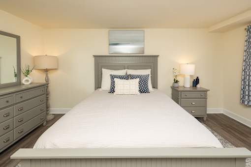 A bedroom with a large bed, two nightstands, and a mirror. at Colony Hill Apartments & Townhomes, Baltimore, MD