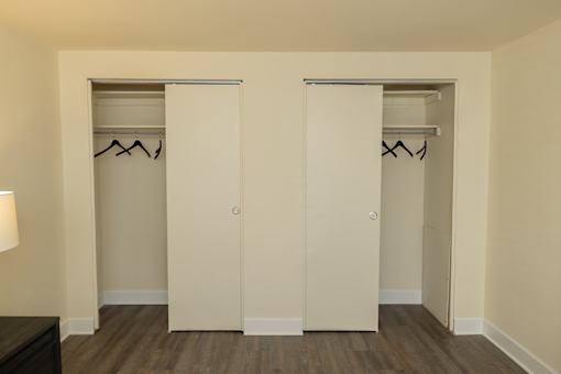 Two white closet doors with clothes hanging on them.