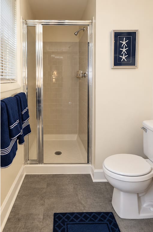 A bathroom with a toilet, a shower with a glass door, and a towel hanging on the wall.