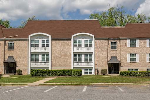 A large brick building with a parking lot in front at The Brittany Apartments, Maryland, 21208