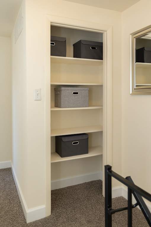 A white shelving unit with three shelves and two storage boxes on the bottom shelf.