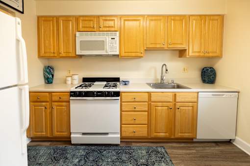 Kitchen with white appliances and wooden cabinets at Rockdale Gardens Apartments*, Baltimore.