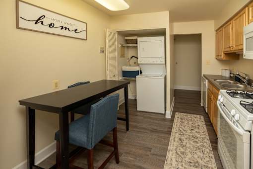 A kitchen with a table and chairs in front of a sign that says Home Sweet Home at The Brittany Apartments, Pikesville, Maryland