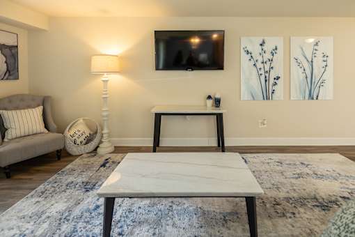 A living room with a grey couch, a white coffee table, a lamp, a TV, and two paintings on the wall.at Deer Park Apartments, Randallstown, MD