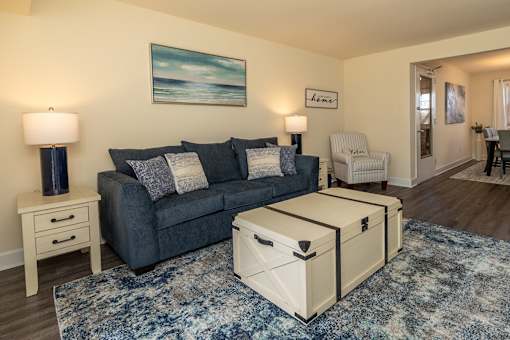 A living room with a grey couch, a white ottoman, and a painting on the wall.