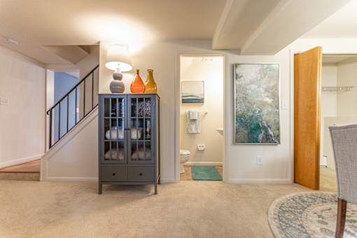 A grey cabinet with bottles on top is in a room with a rug and a painting on the wall.