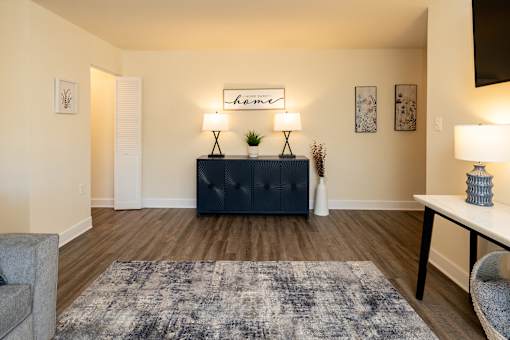 A living room with a grey rug, a white table, a black cabinet, and a lamp.
