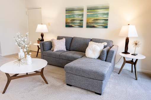 A grey couch with a white pillow on it sits in a living room.