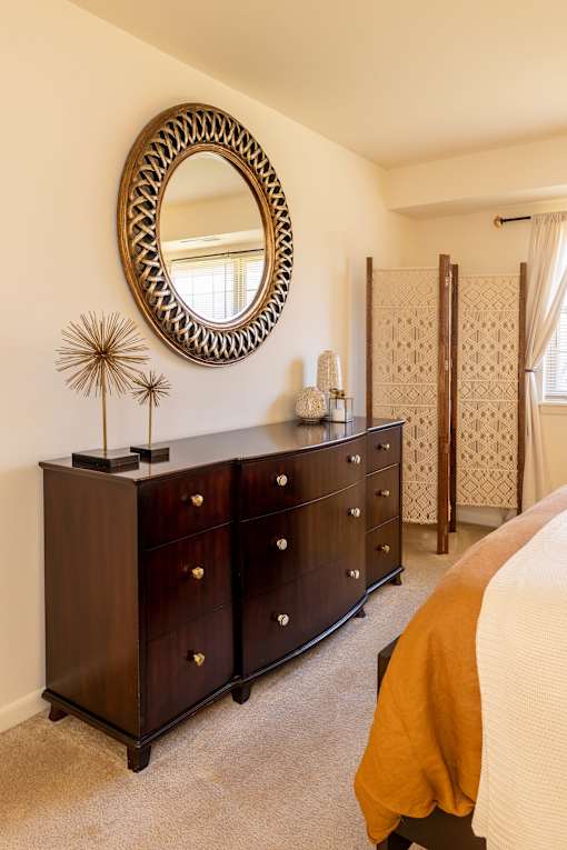 A bedroom with a large mirror and a dark brown dresser.