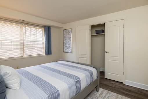 A bedroom with a bed, a window with blinds, and a small closet.
