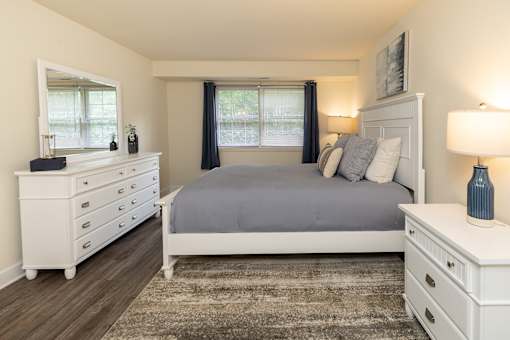 Primary bedroom with queen bed, nightstand, and window at Village of Pine Run Apartments & Townhomes*, Maryland, 21244