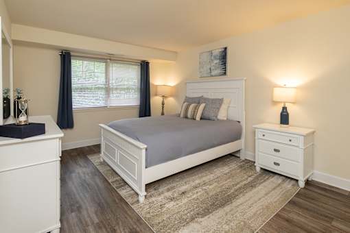 Primary bedroom with queen bed, nightstand, and window
 at Village of Pine Run Apartments & Townhomes*, Maryland, 21244