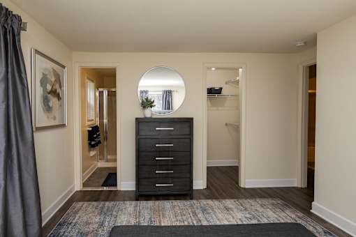A black dresser with a round mirror above it in a room with a grey carpet. Spring Hill Apartments & Townhomes, Baltimore, MD 21234