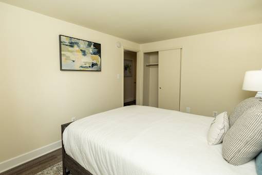 A bedroom with a bed, a painting on the wall, and a lamp.