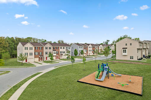 A playground with a green and blue slide in the middle of a grassy area.