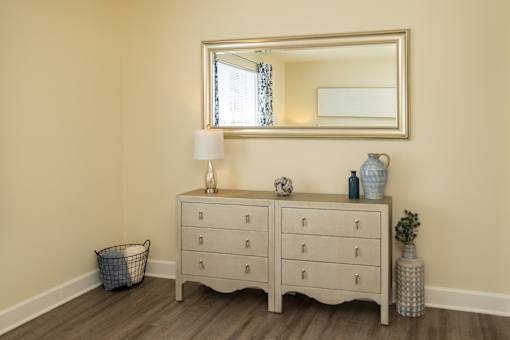 A large mirror hangs over a white dresser with a lamp and vases on top at The Brittany Apartments, Pikesville, MD