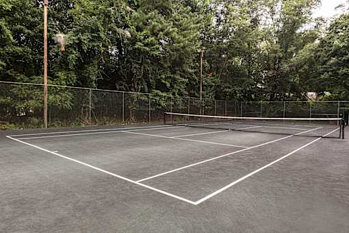 A tennis court surrounded by a fence and trees at The Brittany Apartments, Maryland