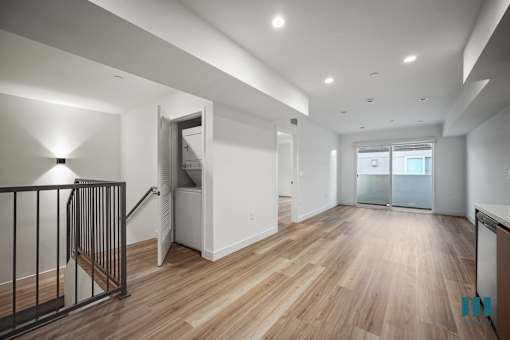 A spacious room with wooden floors and a staircase with a metal railing.