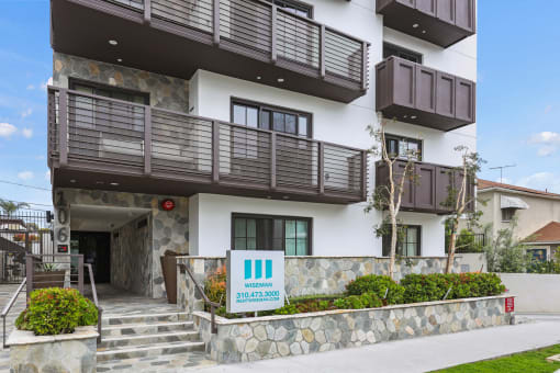 an image of the front of a building with brown balconies and a stone wall in front