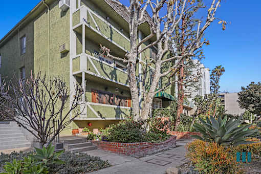 A green building with a balcony and a tree in front.