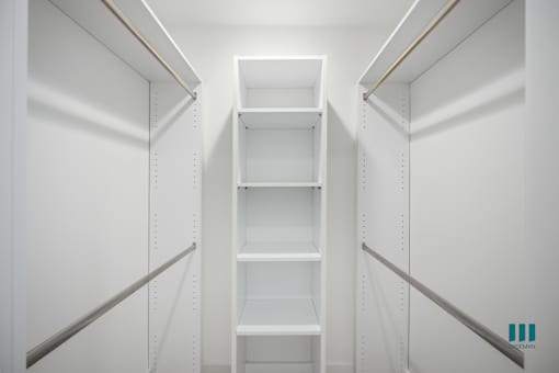A white walk in closet with shelves and a logo in the bottom right corner.