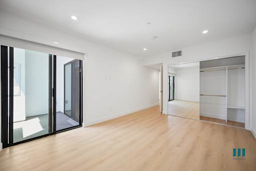 A room with wooden floors and white walls, with a sliding glass door on the left.