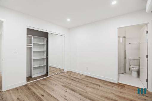 A white room with a wooden floor and a refrigerator in the corner.