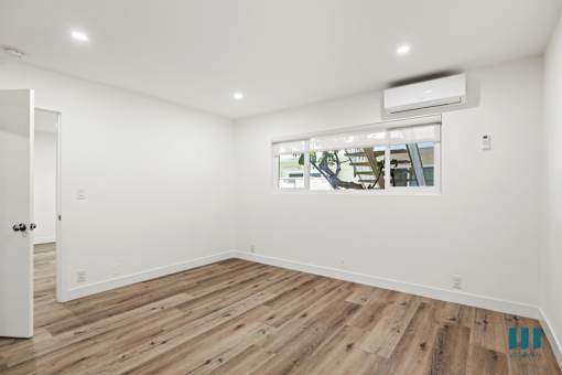 A room with wooden flooring and a window showing an outdoor tree.