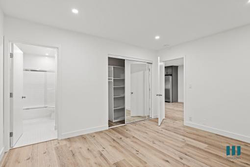 A spacious room with white walls and wooden flooring, featuring a walk-in closet with shelves and a mirror.