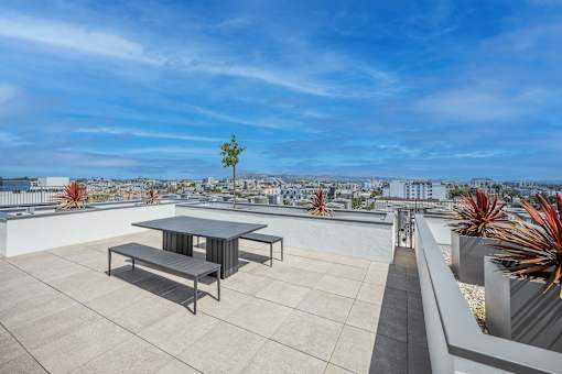 A table and benches are on a rooftop terrace with a view of the city.
