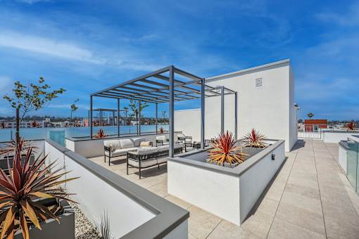 A modern outdoor patio area with a white wall, a couch, and a table.