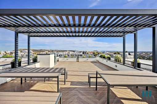 A rooftop patio with wooden floors and benches under a metal pergola.