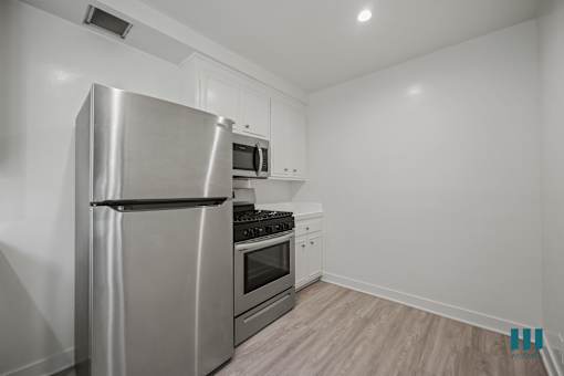 A modern kitchen with a stainless steel refrigerator, microwave, oven, and wooden flooring.