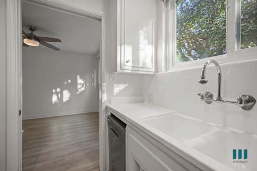 A white bathroom with a sink, mirror, and a fan.
