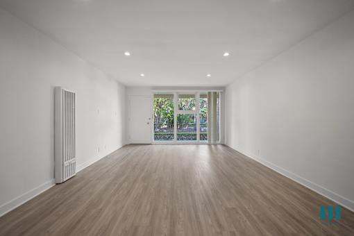A spacious room with wooden flooring and a window with a view of greenery outside.