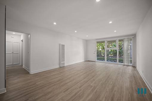 A spacious room with wooden flooring and a sliding glass door leading to a balcony.