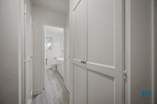 A hallway with white walls and wood flooring.