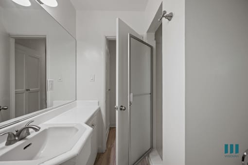A bathroom with a sink, mirror, and shower.